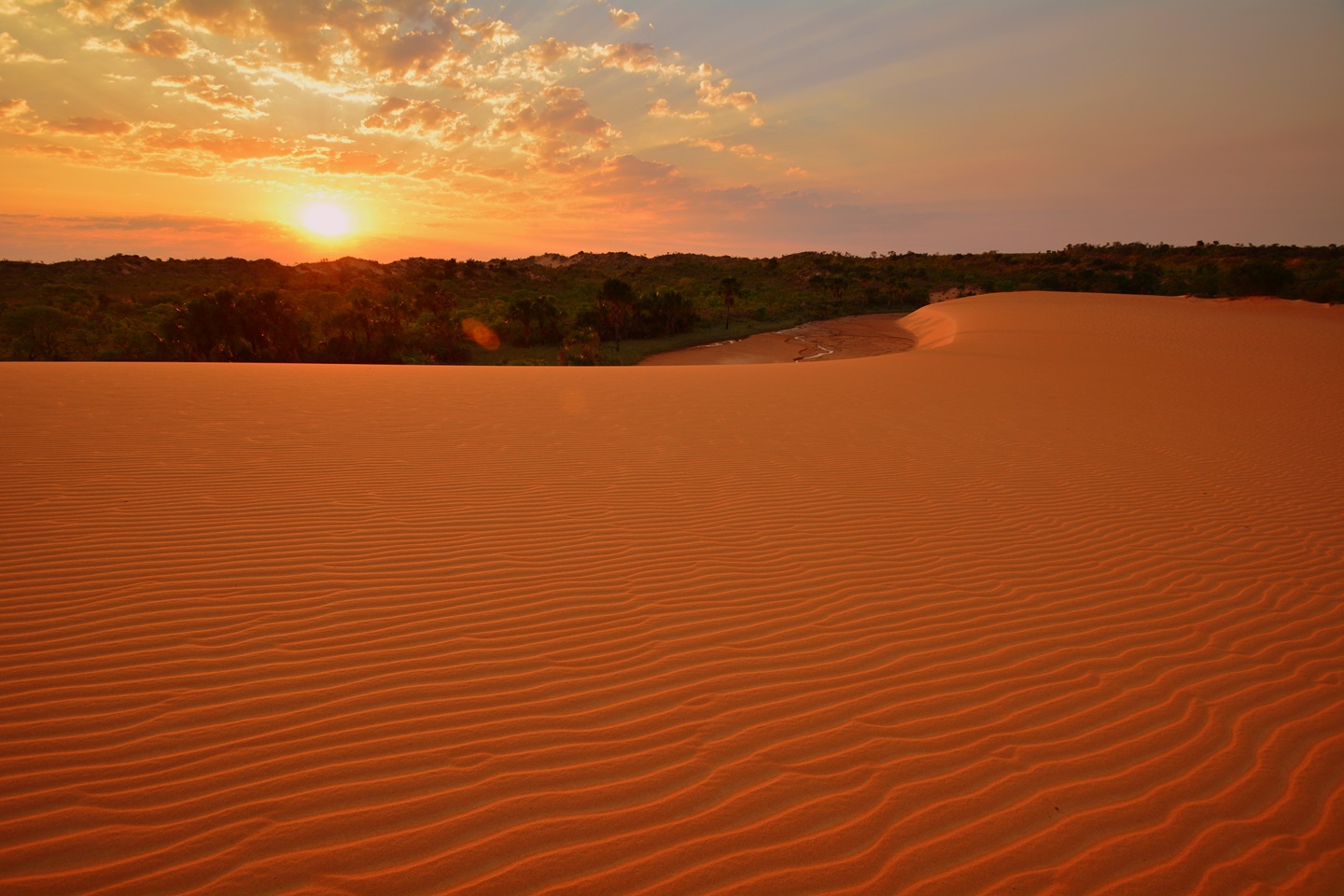 Duna de areia clara e alaranjada do Jalapão ao entardecer, em Mateiros, com a vegetação de cerrado ao fundo e o céu em tons quentes