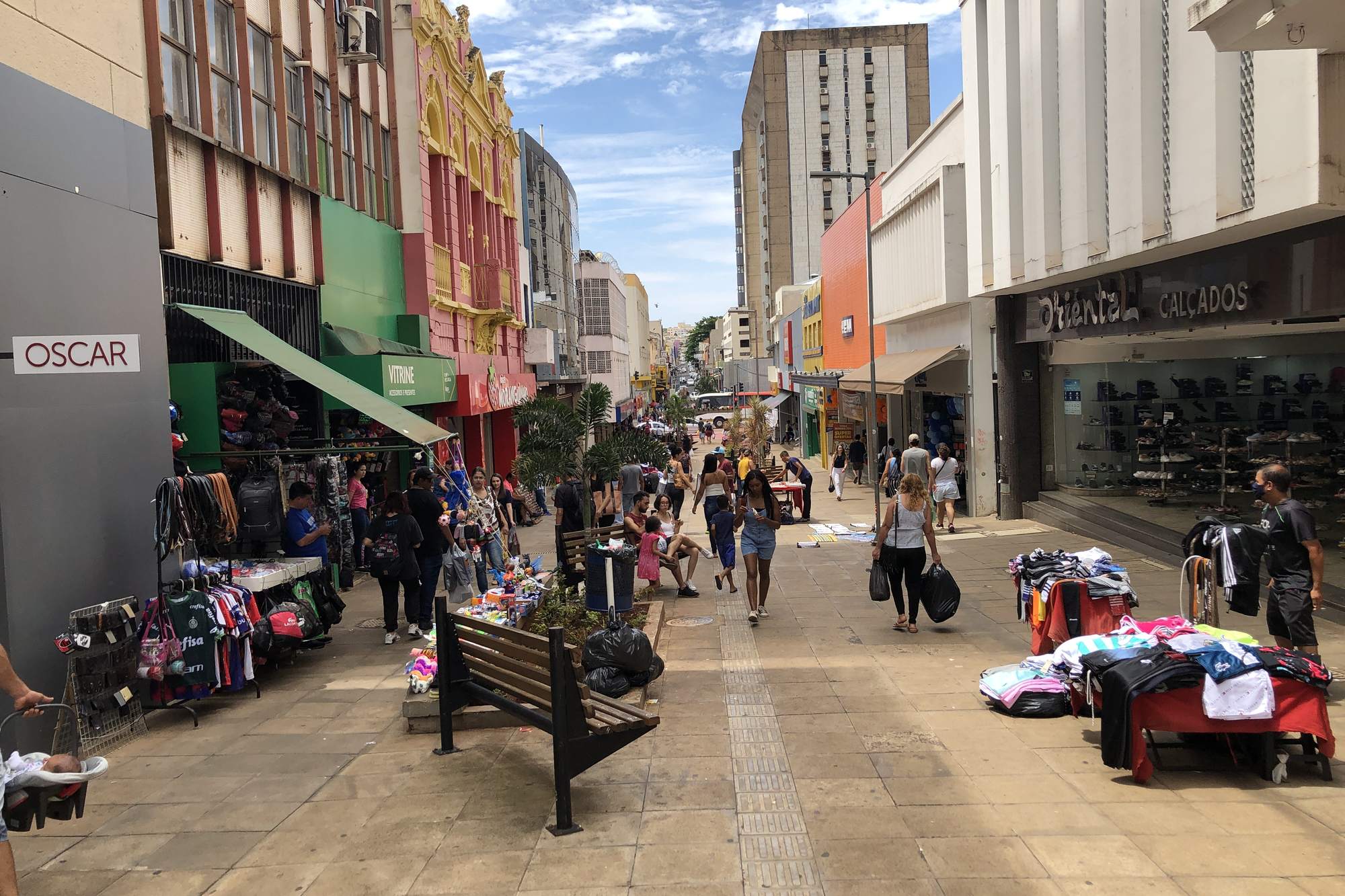 Rua de pedestres no Centro de Uberaba com gente fazendo compras e bancas de roupa na calçada.