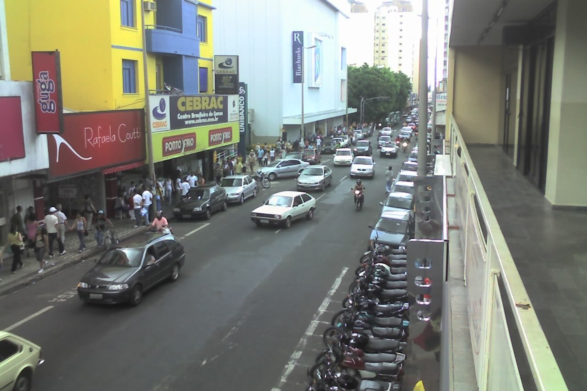 Rua comercial do Centro de Uberlândia com pedestres nas calçadas, lojas e motos estacionadas.
