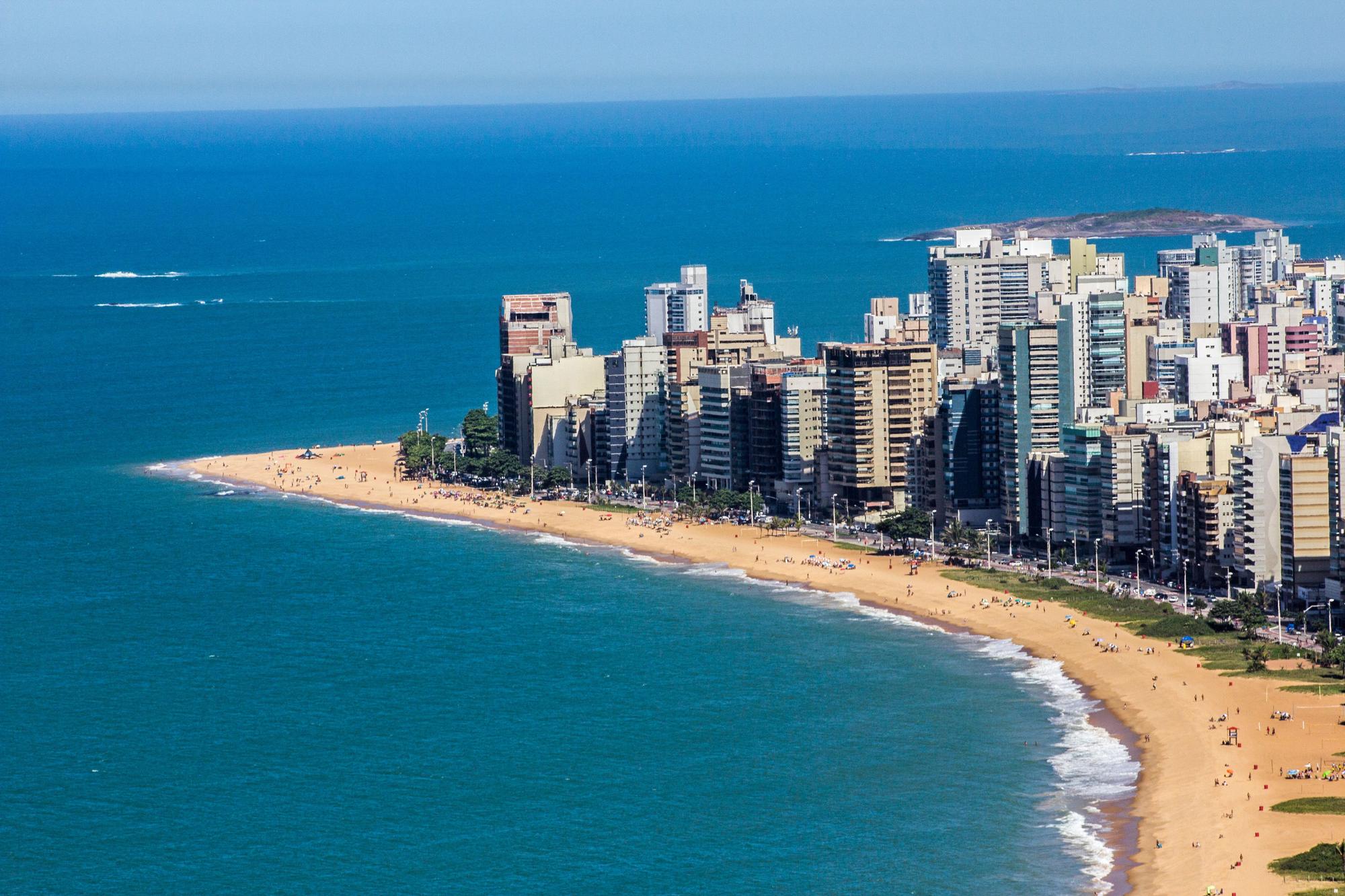 Orla de Vila Velha vista do alto, com banhistas na areia e os prédios altos da praia.