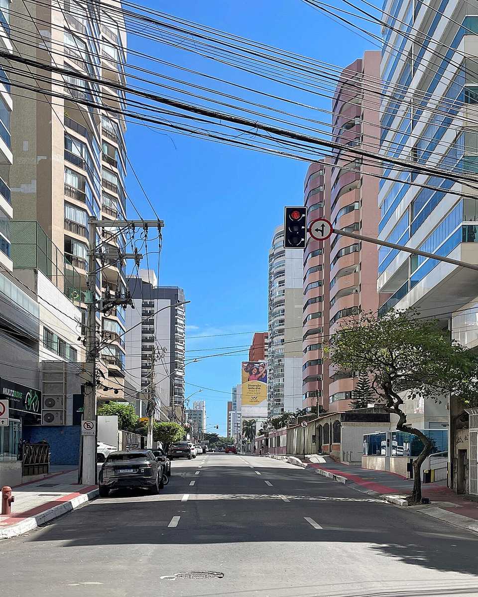 Rua do bairro de Itapoã com prédios residenciais dos dois lados, comércio térreo e bicicletas de aluguel na calçada.
