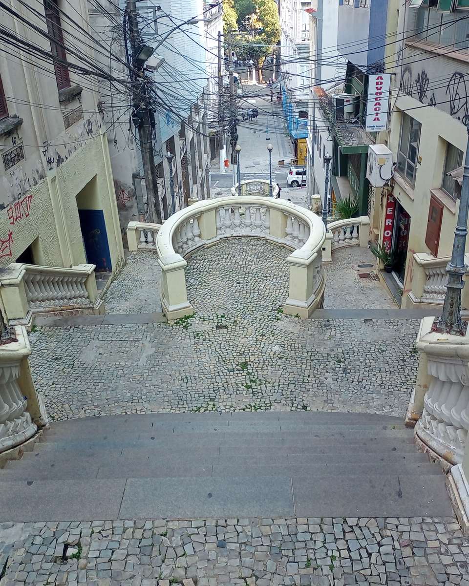 Escadaria Maria Ortiz vista do alto, com os degraus de pedra descendo entre os casarões do Centro de Vitória até a rua movimentada lá embaixo.